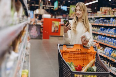 Müşteri akıllı bir telefon kullanıyor ve markette alışveriş arabasıyla alışveriş yapıyor.