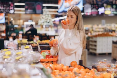 Bir süpermarketin meyve ve sebze reyonundan alışveriş yaparken hurma kokusu alan genç bir kadın.