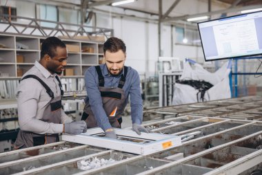 İki fabrika işçisi bir üretim hattında alüminyum pencere çerçevesini birleştiriyor ve kaliteyi sağlamak için birlikte çalışıyorlar.