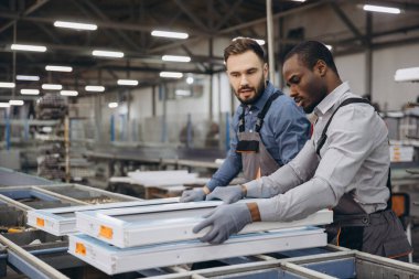 Modern bir pencere ve kapı üretim tesisinde alüminyum ve pvc pencere çerçevelerini dikkatlice kullanan iki fabrika işçisi