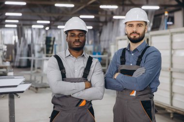 Üniformalı ve kasklı iki mühendis alüminyum ve PVC pencere ve kapı üretim fabrikalarında kesişiyor.