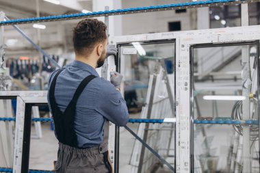 Alüminyum ve pvc pencere çerçevelerini üretim hattında birleştiren koruyucu eldivenler giyen fabrika işçisi