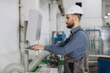 Üniforma giyen ve bilgisayar kullanan fabrika işçisi alüminyum ve pvc pencere ve kapı üretimi için kontrol mekanizması kullanıyor.