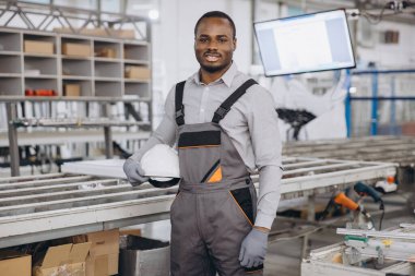 Beyaz miğferi alüminyum ve pvc pencere ve kapı üretim hattında tutan Afrikalı Amerikalı fabrika işçisi