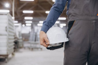 Alüminyum, PVC pencere ve kapı üretiminde uzmanlaşmış bulanık bir endüstriyel ortamda elinde beyaz bir kaskla çalışan bir fabrika işçisine yakın plan.