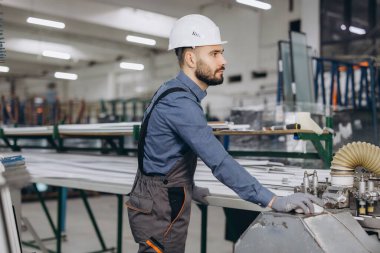 Üniforma giyen ve sanayi makineleri kullanan fabrika işçisi alüminyum, pvc pencere ve kapı üretiyor.