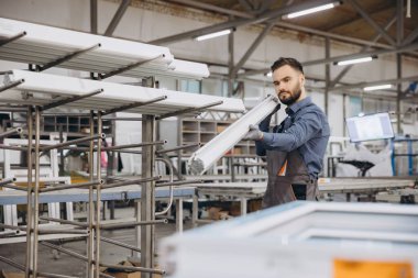 Alüminyum ve pvc pencere ve kapı üretiminde uzmanlaşmış bir fabrikada pvc pencere çerçevesi taşıyan fabrika işçisi