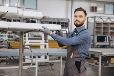 Eldiven giyen fabrika işçisi, pencere ve kapı yapımı için atölyedeki raflardan alüminyum profil çıkarıyor.