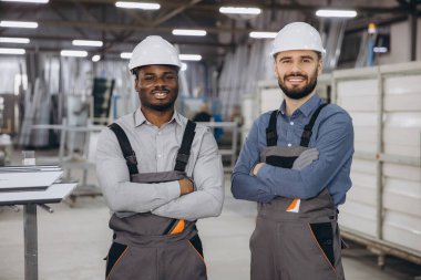 Alüminyum, pvc pencere ve kapı üretiminde uzmanlaşmış marangozluk atölyesinde kolları kavuşturulmuş gülümseyen iki fabrika işçisi.