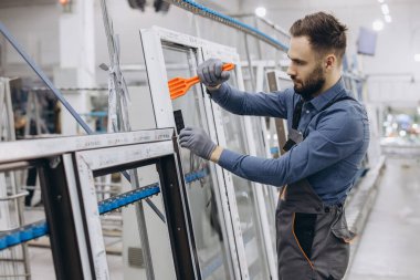 Bir pencere ve kapı fabrikasında yeni bir alüminyum ve pvc pencere çerçevesi monte eden fabrika işçisi