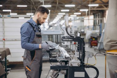 Eldiven takan fabrika işçisi panoya not alırken aynı zamanda alüminyum, pvc pencere ve kapı üretimi için endüstriyel makineler kullanıyor.