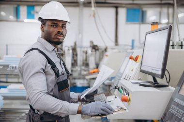 African american factory worker operating machinery and reading instructions for aluminum and PVC windows and doors production clipart