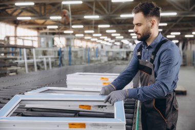 Eldiven takan fabrika işçisi bir pencere fabrikasında üretim hattına PVC pencere çerçeveleri yerleştiriyor.