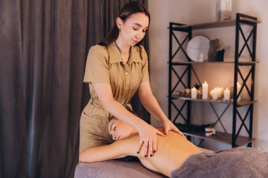 Profesyonel masöz, spa merkezinde kadının sırtına mumlarla masaj yapıyor.