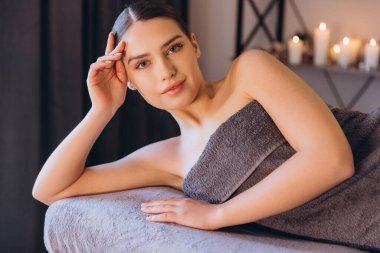 Yumuşak gri bir havluya sarılmış, masaj masasında uzanmış, huzurlu bir kaplıca ortamında gençleştirici bir sağlık tedavisinin tadını çıkaran rahat bir kadın.