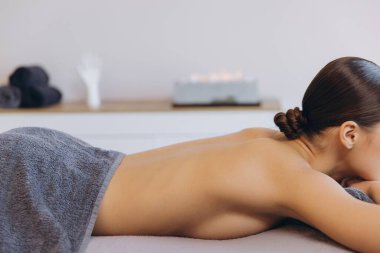 Profesyonel masaj alan bir kadın, yastıklı masaya yüzüstü uzanmış, sakin bir spa sağlık tedavisi görüyor.