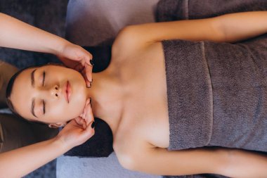 Güzellik uzmanı masaj masasında uzanan ve güzellik merkezinde rahatlatıcı tedavinin keyfini çıkaran genç bir kadın.