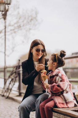 Anne ve kızı parkta otururken dondurma yiyorlar, gülümsemelerini paylaşıyorlar ve şehirde neşeli anılar yaratıyorlar.