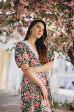 Büyüleyici bahar mevsimi boyunca canlı pembe taç yapraklarıyla çevrili çarpıcı bir kiraz ağacının altında zarif poz veren modaya uygun bir model.