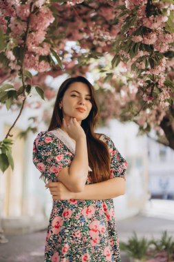 Sakura dallarının altında zarif bir şekilde poz veren model canlı pembe çiçeklerle süslenmiş, bahar zamanının güzelliğini somutlaştırıyor.