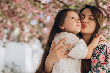 Anne ve kızı, çiçek açan bir kiraz ağacının altında, doğanın güzelliğinin ve bağlarının sıcaklığının tadını çıkararak hassas bir anı paylaşıyorlar.