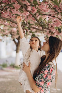 Anne ve kızı, bahar çiçeklerinin güzelliğiyle çevrili çiçek açan kiraz ağacının altında neşeli bir anı paylaşıyorlar.