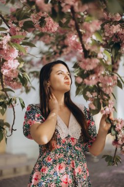 Baharda çiçek açan bir sakura ağacının yanında zarif poz veren manken, canlı pembe çiçeklerin hoş kokusunun tadını çıkarıyor.