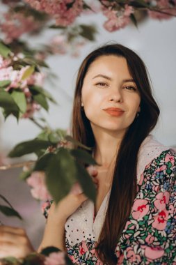 Çekici genç bir kadın güzel bir bahar bahçesinde çiçek açan sakura çiçeklerinin tadını çıkarıyor, neşe ve sükunet saçıyor.