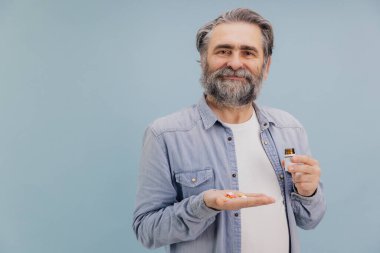 Kendine güvenen sakallı yaşlı bir adamın portresi ilaç ve ilaç şişesi gösteriyor, yaşlılıkta sağlık ve sağlığı destekliyor.