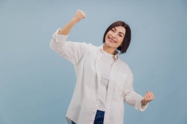 Mutluluk ve zaferi ifade eden mutlu kadın, başarıyı yumruklarıyla kutluyor, neşeyle gülümsüyor, coşku ve olumlu duygular gösteriyor.