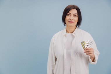 Orta yaşlı kadın elinde çeşitli ilaç paketleri tutuyor, etkili hastalık tedavisi ve sağlık çözümlerini destekliyor