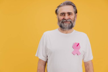 Göğüs kanserini destekleyen pembe kurdele takan gülümseyen son sınıf öğrencisinin portresi, sarı arka planda duruyor.