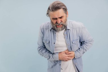 Karnı ağrıyan sakallı olgun bir adamın portresi. İki eliyle karnını tutuyor. Mavi arka planda rahatsızlık ve acı gösteriyor.
