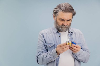 Endişeli kıdemli bir adam ilaç paketinde ilaç talimatlarını okurken ilaç tedavisi ve tedavisi hakkında endişe ve kafa karışıklığı gösteriyor.