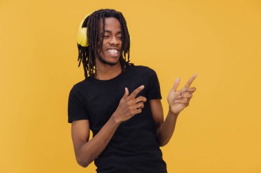 Sarı kulaklık takan genç Afrikalı Amerikalı müzik dinliyor ve sarı arka planda gülümseyerek dans ediyor.