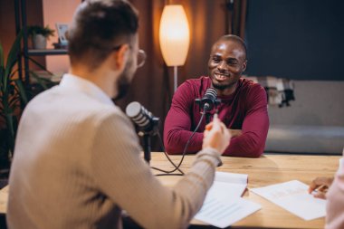 İki podcaster bir stüdyoda konuşuyorlar ve ses içeriğini kaydediyorlar. Düşüncelerini mikrofonlarla tartışıp paylaşıyorlar.