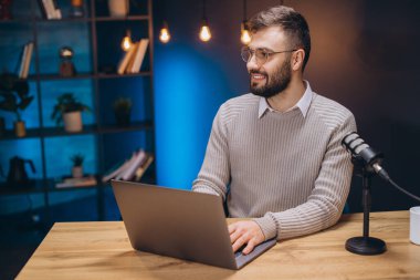 Milenyum Podcaster 'ı evde çalışıyor, kulaklık takıyor, mikrofona konuşuyor ve bilgisayarda dijital ses içeriğini kaydediyor.