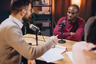 İki radyo sunucusu bir stüdyo podcast 'inde bir konukla röportaj yapıyor, fikirleri tartışıyor ve paylaşıyor.