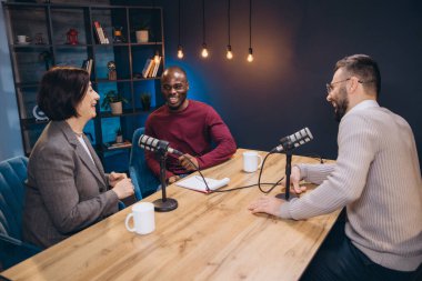 Podcaster 'lar, modern ekipmanlarla dolu canlı ve profesyonel bir stüdyoda yeni bir bölüm çekerken kahkaha ve bağlantının keyfini çıkarıyorlar.