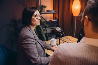 Profesyonel podcasterlar ses kayıtlarını kaydediyor, kulaklık takıyor, mikrofon ve dizüstü bilgisayarla lüks stüdyo masasında çalışıyor.