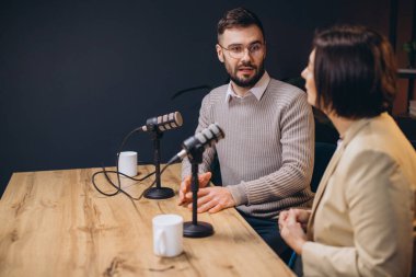 Profesyonel ekipmanlarla çevrili modern bir stüdyoda ses içeriğini kaydederken canlı sohbetler yapan iki podcaster.