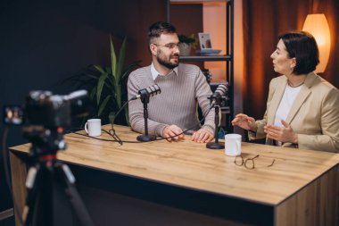 Podcasters ses segmenti kaydediyor, modern stüdyo ortamında profesyonel ses ekipmanlarıyla mikrofonlara konuşuyor