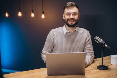 Genç podcaster ses içeriğini kaydediyor, modern stüdyo ortamında profesyonel mikrofonla çalışıyor.