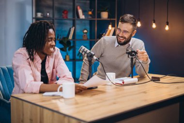 Profesyonel bir stüdyoda yeni bir podcast bölümü çekerken gülüp eğlenen iki erkek podcaster.