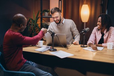 Üç podcaster bir bölüm kaydederken başarılarını kutluyorlar. Heyecan ve takım çalışmasıyla dolu bir stüdyoda yumruk tokuşturuyorlar.