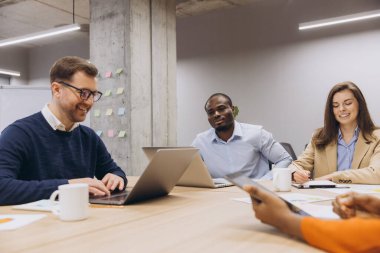 Çeşitli profesyonel ekip konferans masası etrafında işbirliği yapıyor, belgeleri gözden geçiriyor ve modern işyeri ortamında dijital cihazlar kullanarak stratejiyi tartışıyor