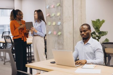Modern ortak çalışma alanındaki proje stratejisini tartışan ekip üyeleri tarafından yoğun bir şekilde dizüstü bilgisayarda çalışan profesyonel