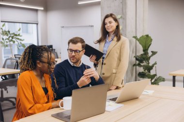 Teknoloji ve yeşillik ile çevrili modern bir ofis ortamında çeşitli profesyonel gruplar ortak bir tartışmaya girişiyor.