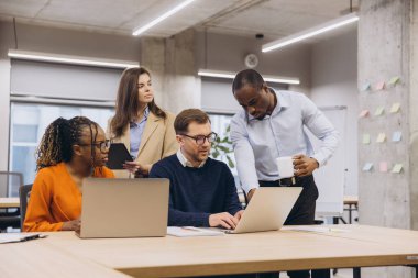 Çağdaş bir ofiste birlikte çalışan, fikirleri tartışan ve teknolojiyi üretkenliği ve işbirliğini geliştirmek için kullanan bir grup profesyonel.