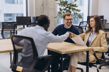 Proje detaylarını tartışan profesyoneller, modern çalışma ortamında cam duvarlar ve parlak mobilyalarla yapılan takım toplantılarında dikkatle işbirliği yapıyorlar.